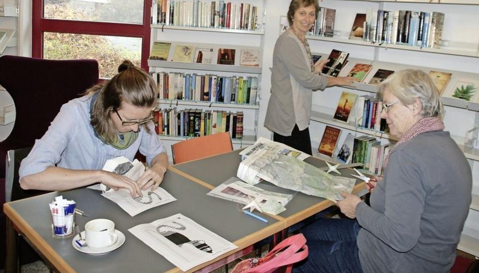 Barbara Eichholzer (links) faltet ein Buch, sodass am Schluss im Beschnitt der Buchseiten eine Katze zu sehen ist. In der Mitte Bibliotheksleiterin Rita Schneider, die den Workshop organisierte. Vreni Frischknecht zerschneidet eine Landkarte. (Bild Alfred Wüger)