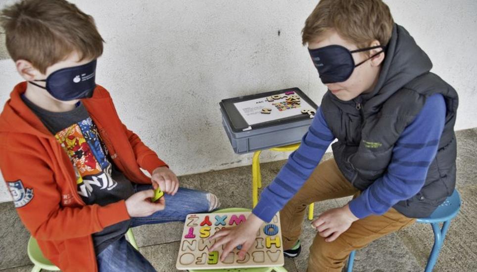 Gar nicht so einfach: Mit verbundenen Augen versuchen Hallauer Primarschüler, hölzerne Buchstaben in die richtigen Vertiefungen einzufügen. Bild: Theo Kübler