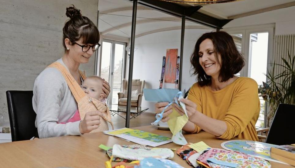 Lia Macello (rechts) besucht seit Frühling junge Familien zu Hause. Die Besuche sind eine von 17 beschlossenen Frühförderungsmassnahmen. Im Bild suchen Alexandra Fetz und Tochter Emma ein Geschenk aus – ein von Neuhauser Schülern genähtes Lätzchen. Bild: Selwyn Hoffmann