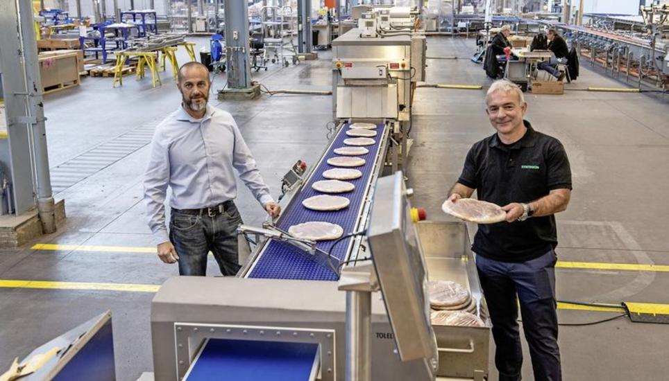 Projektleiter Sergej Reisenhauer (l.) und Standortleiter Bruno Oberle neben dem Förderband des 100 Meter langen Pizza-Verpackungssystems. Bild: Daniel Thüler