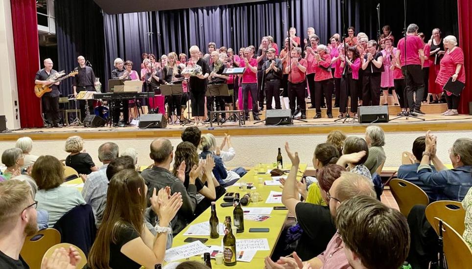 Da klatscht nicht nur das Publikum, sondern auch der Chor. Vreni Winzeler (mit Geschenk) hat alle mit einem feurigen Konzertabend beglückt. Bild: Gudrun Trautmann