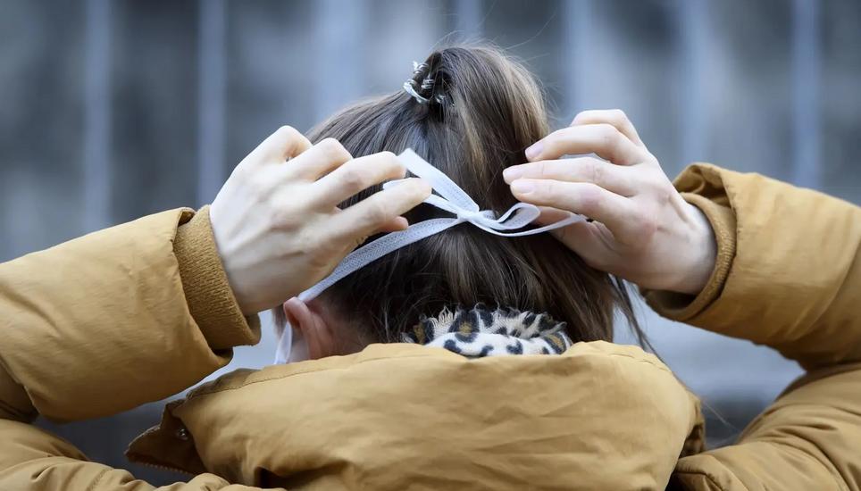 Eine Frau, die gerade in ein Spital eintreten will, befestigt eine Schutzmaske. Bild: Anthony Anex/Keystone