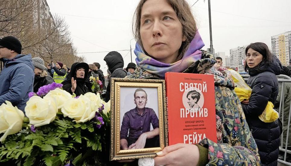 «Ein Heiliger gegen ein Reich» ist der Titel des Buches, das diese Frau an der Beerdigung neben einem Bild Alexej Nawalnys hält. Bilder: Key A woman holds a portrait of Alexei Navalny and a book titled "A saint against the Reich" as people gather outside the Church of the Icon of the Mother of God Soothe My Sorrows, in Moscow, Russia, Friday, March 1, 2024. Relatives and supporters of Alexei N