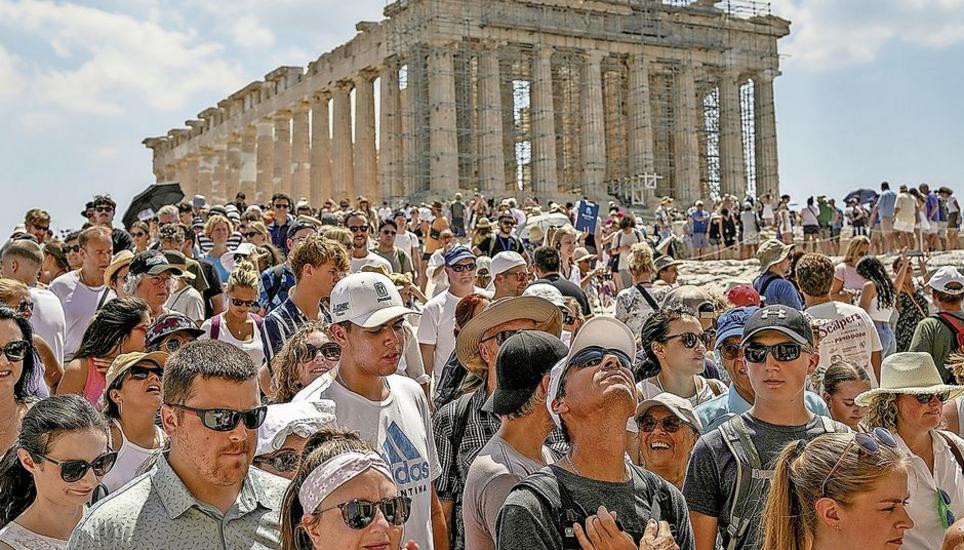 Atop the Acropolis ancient hill, tourists visit the Parthenon temple, background, in Athens, Greece, Tuesday, July 4, 2023. Crowds are packing the Colosseum, the Louvre, the Acropolis and other major attractions as tourism exceeds 2019 records in some of 