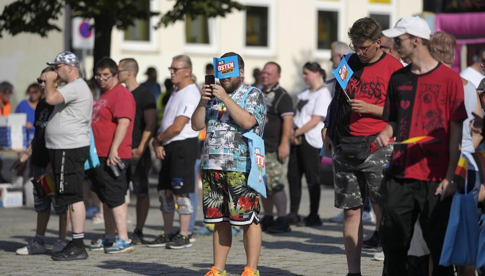 Supporters of the far-right Alternative for Germany party, or AfD, hold small paper flags that read: "The East Does it", as they attend an election campaign rally of the party for upcoming state elections in Suhl, Germany, Tuesday, Aug. 13, 2024. In the f