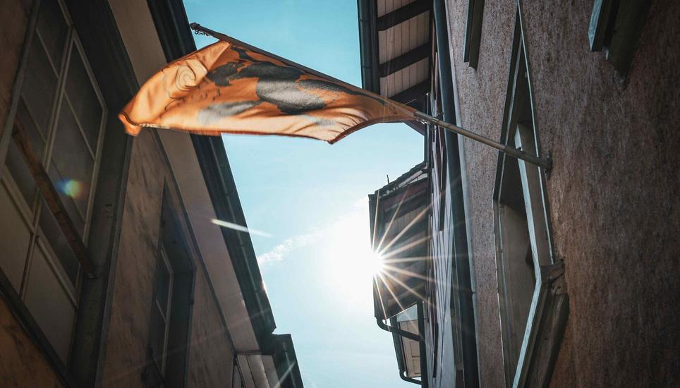 Die Schaffhauserinnen und Schaffhauser können sich auf eine frühlingshafte Woche mit viel Sonne freuen. Bild: Melanie Duchene Eine Schaffhauser Fahne flackert im Sonnenlicht in einer Gasse mitten in der Schaffhauser Unterstadt, am Montag, 16 Oktober 2023. (Melanie Duchene / Schaffhauser Nachrichten)