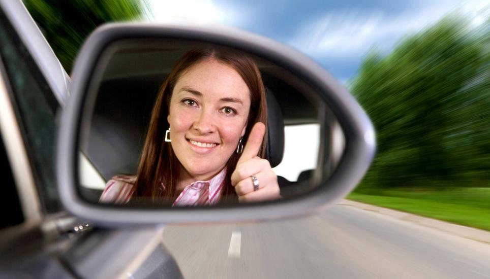woman driving a car on a road with thumbs up in the mirror