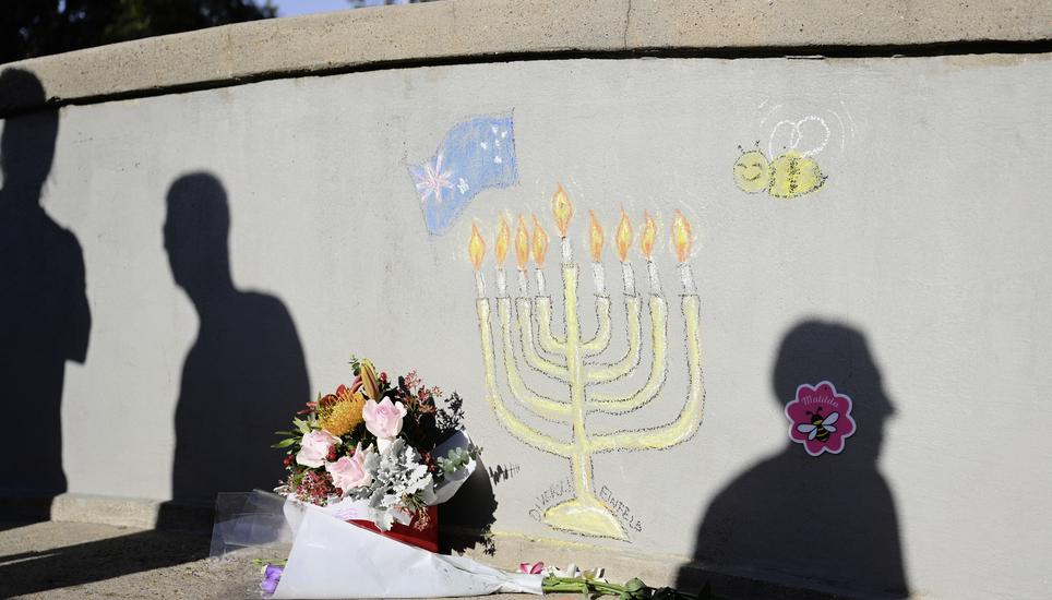 People walk past a memorial drawn on the wall of a walk bridge as a tribute following last Sunday's shooting at Bondi Beach, in Sydney, Friday, Dec. 19, 2025. (AP Photo/Steve Markham)
