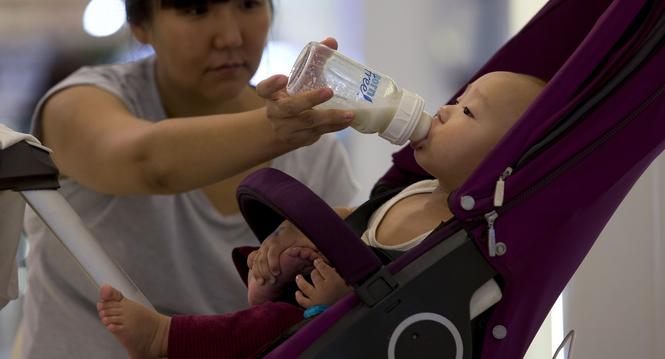 A woman feeds milk to her baby on a stroller at a shopping mall in Beijing, China, Wednesday, Aug. 7, 2013. China announced Wednesday it has fined six milk suppliers, including Mead Johnson and New Zealand's Fonterra, a total of $108 million for price-fix