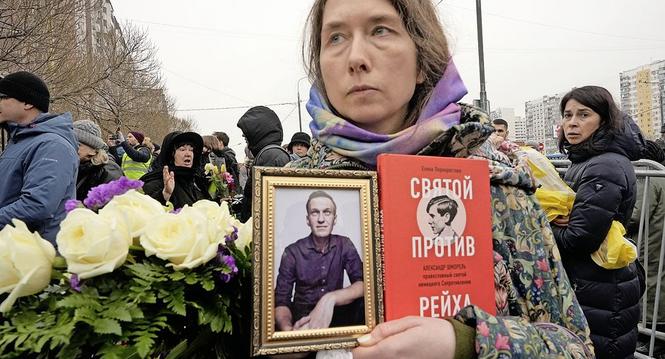 A woman holds a portrait of Alexei Navalny and a book titled "A saint against the Reich" as people gather outside the Church of the Icon of the Mother of God Soothe My Sorrows, in Moscow, Russia, Friday, March 1, 2024. Relatives and supporters of Alexei N