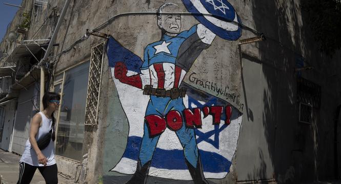 CORRECTS TO WOMAN - A woman walks past a mural depicting U.S. President Joe Biden as a superhero defending Israel on a street in Tel Aviv, Israel, Sunday, April 14, 2024. Israel on Sunday hailed its successful air defenses in the face of an unprecedented 