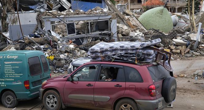 Displaced residents returning to their village, sit in their car with belonging as they pass in front of a destroyed mosque, in the town of Bint Jbeil, southern Lebanon, following a ceasefire between Israel and Hezbollah that went into effect on Wednesday