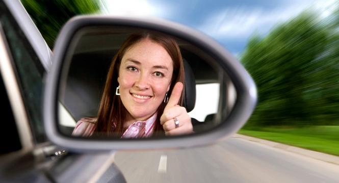 woman driving a car on a road with thumbs up in the mirror